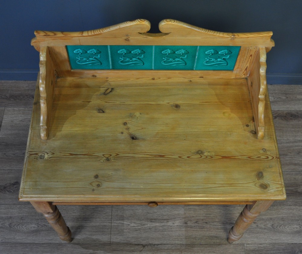 An antique Victorian pine washstand featuring a raised gallery splashback set with four green embossed tiles, a single frieze drawer, and turned legs. View VI