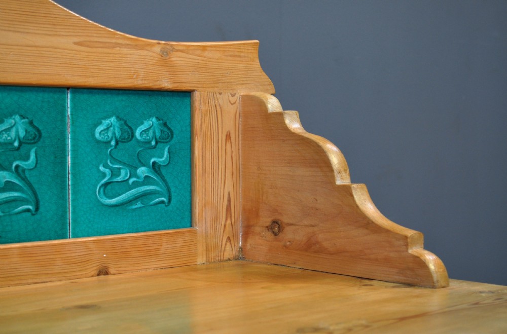 An antique Victorian pine washstand featuring a raised gallery splashback set with four green embossed tiles, a single frieze drawer, and turned legs. View VIII