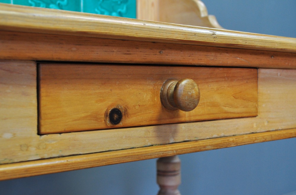 An antique Victorian pine washstand featuring a raised gallery splashback set with four green embossed tiles, a single frieze drawer, and turned legs. View XI