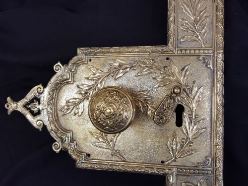 fig 1. An ornate Regency period cast brass door plate featuring raised botanical leaf decoration, a round decorative door knob, a keyhole escutcheon, and ornate cresting.