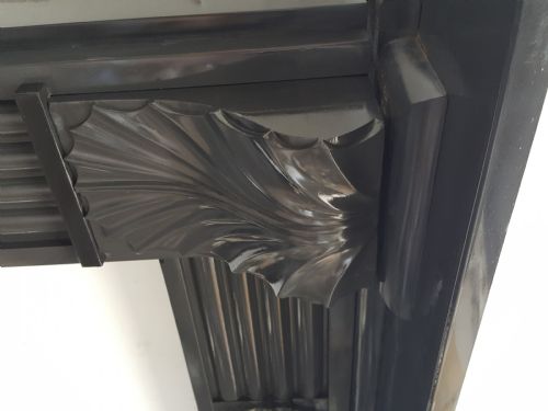 fig 2. A black Victorian Welsh slate fireplace surround featuring fluted side jambs, carved fan brackets, and a central floral rosette motif.
