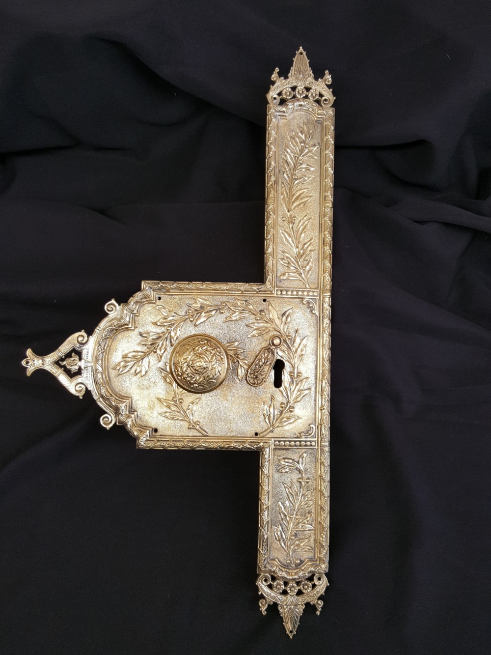 An ornate Regency period cast brass door plate featuring raised botanical leaf decoration, a round decorative door knob, a keyhole escutcheon, and ornate cresting.
