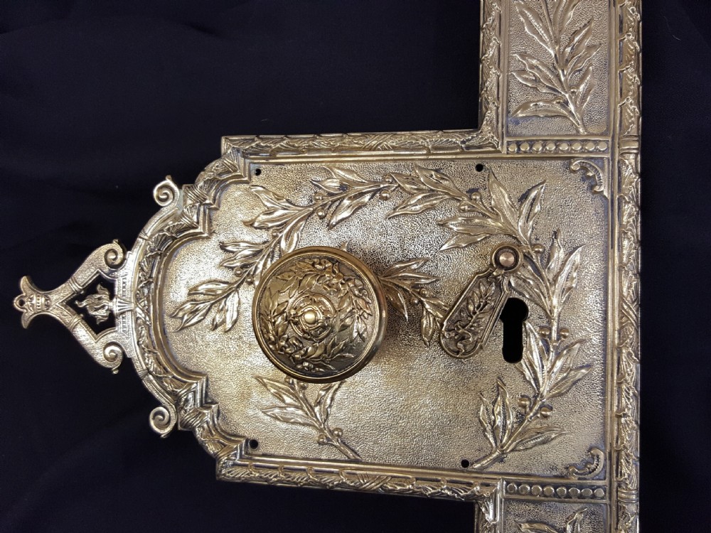 An ornate Regency period cast brass door plate featuring raised botanical leaf decoration, a round decorative door knob, a keyhole escutcheon, and ornate cresting. View II