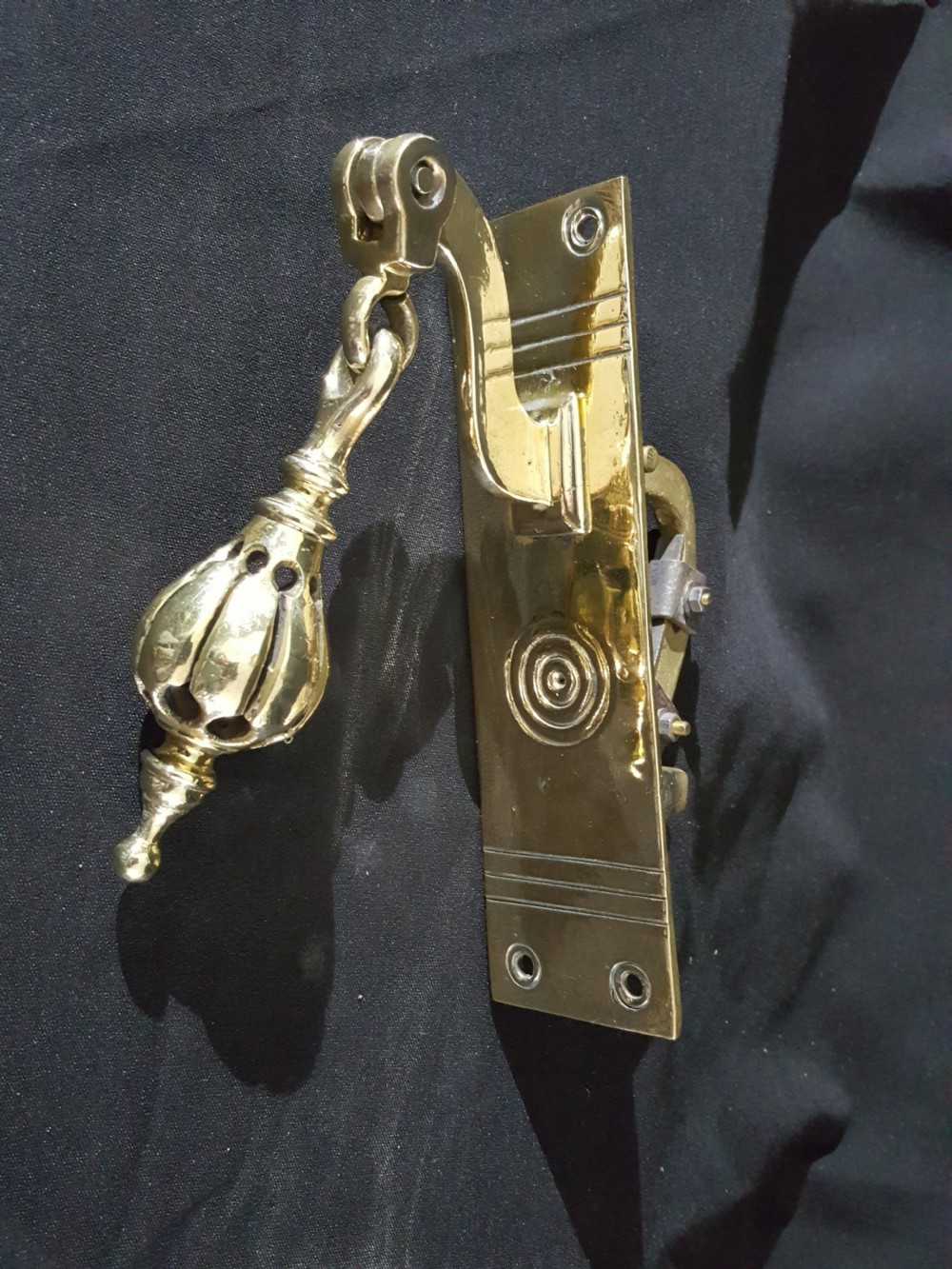 A polished brass Georgian style pull bell mechanism featuring an openwork teardrop handle and rectangular backplate with mounting holes.
