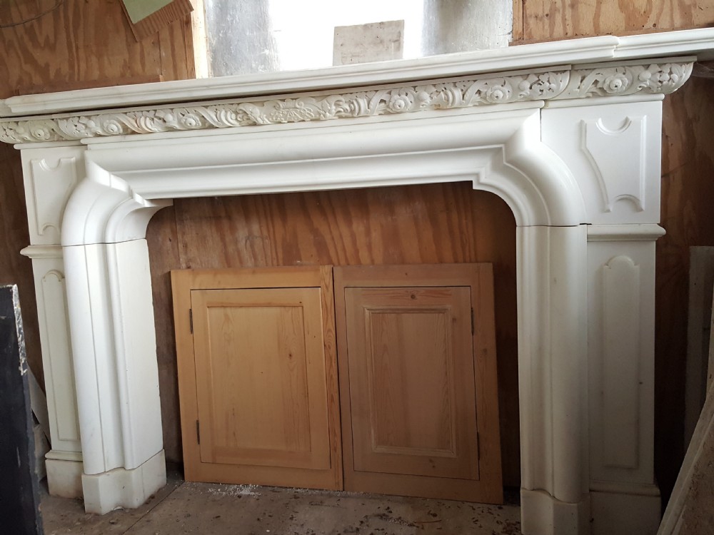 A carved white statuary marble Victorian fireplace surround featuring an ornate floral frieze and moulded arched jambs.