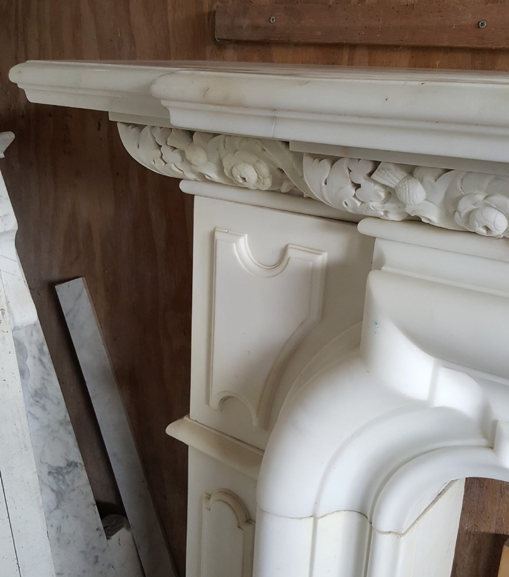 A carved white statuary marble Victorian fireplace surround featuring an ornate floral frieze and moulded arched jambs. View V