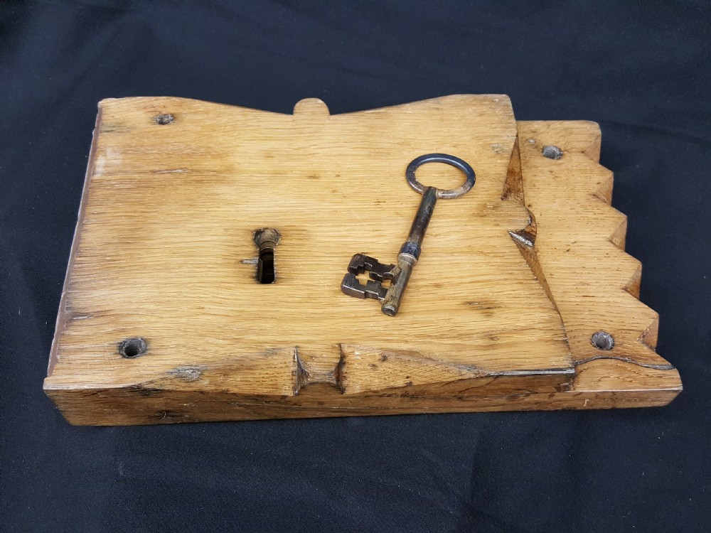 A rectangular Georgian oak wooden stock lock featuring an open keyhole and an accompanying wrought iron key resting on the timber surface.