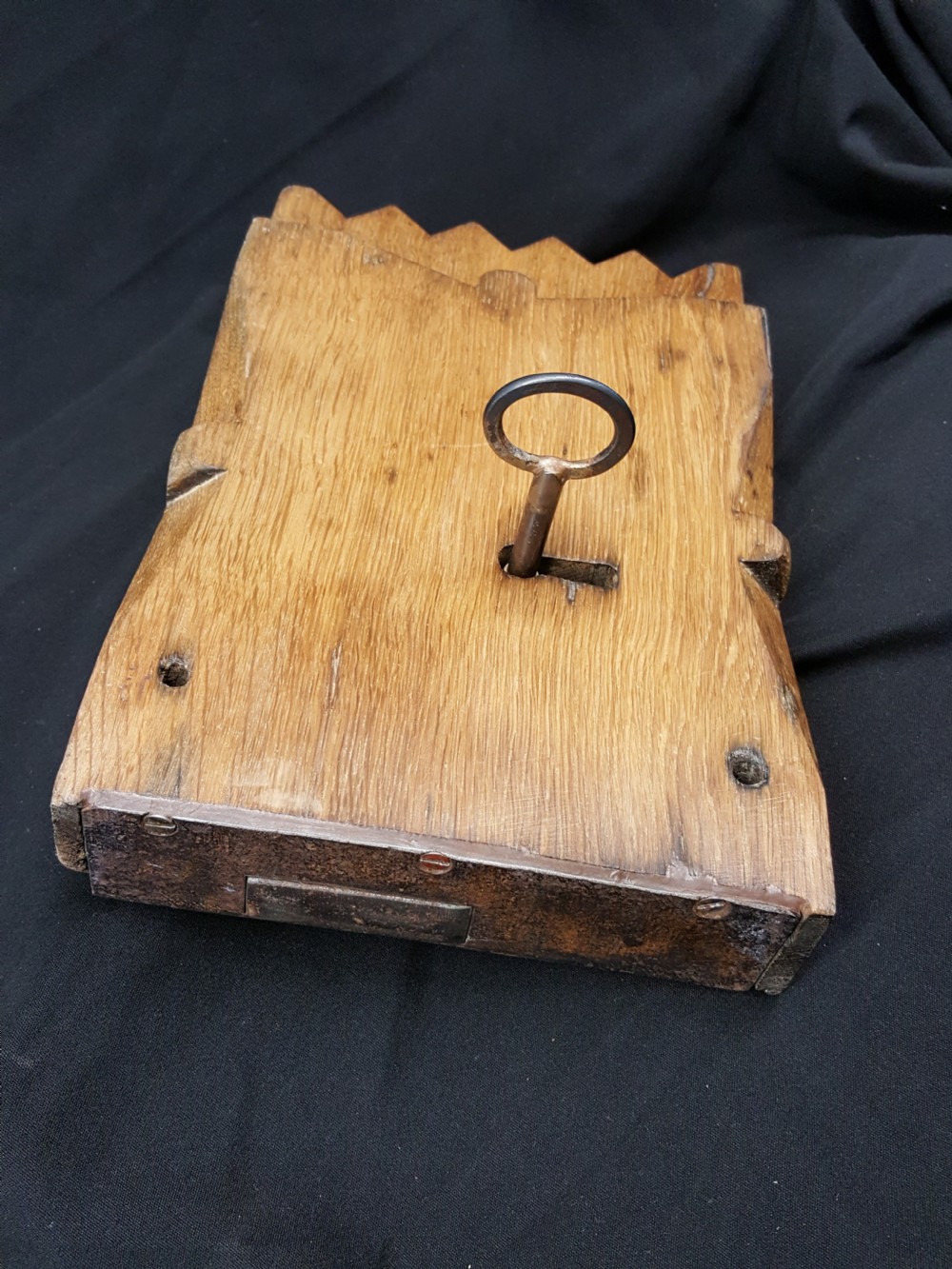 A rectangular Georgian oak wooden stock lock featuring an open keyhole and an accompanying wrought iron key resting on the timber surface. View II