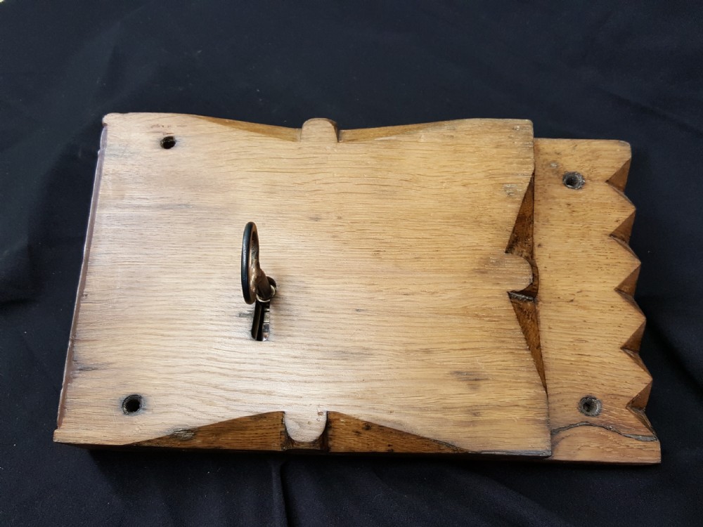 A rectangular Georgian oak wooden stock lock featuring an open keyhole and an accompanying wrought iron key resting on the timber surface. View III