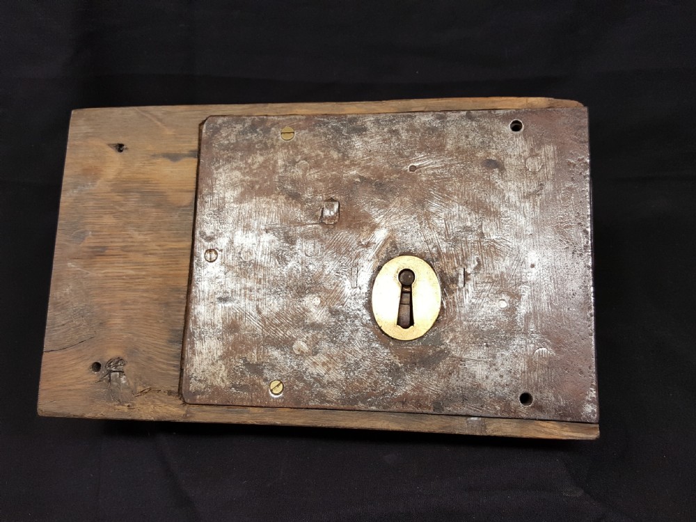 A rectangular Georgian oak wooden stock lock featuring an open keyhole and an accompanying wrought iron key resting on the timber surface. View V