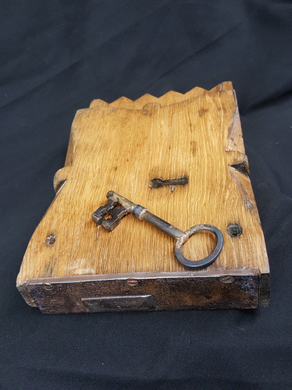 A rectangular Georgian oak wooden stock lock featuring an open keyhole and an accompanying wrought iron key resting on the timber surface. View VI