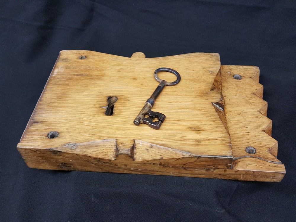 A rectangular Georgian oak wooden stock lock featuring an open keyhole and an accompanying wrought iron key resting on the timber surface. View VII