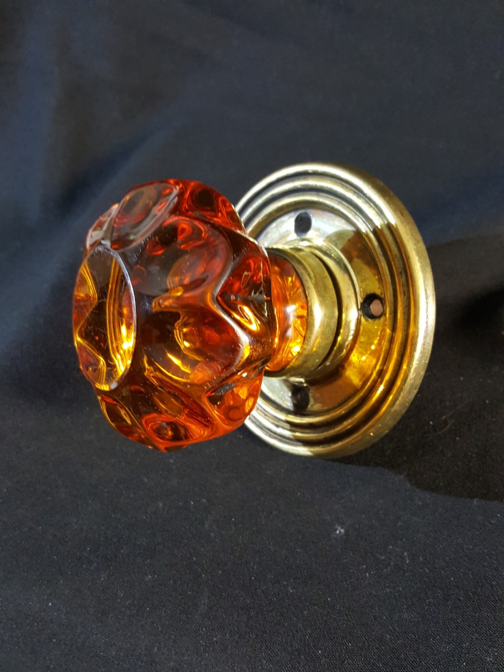 A Victorian amber glass door knob with a faceted profile mounted on a circular stepped brass backplate.