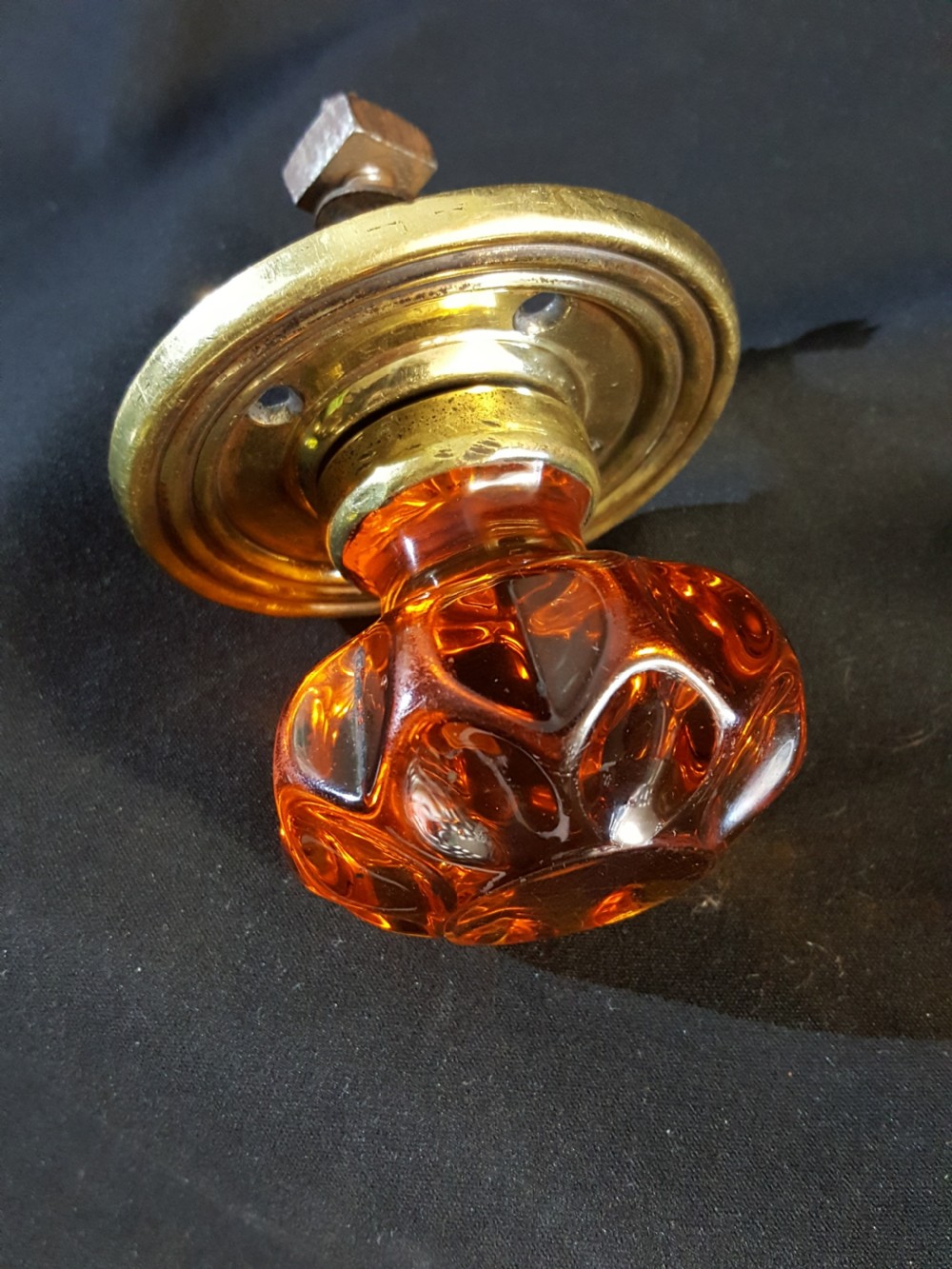 A Victorian amber glass door knob with a faceted profile mounted on a circular stepped brass backplate. View IV