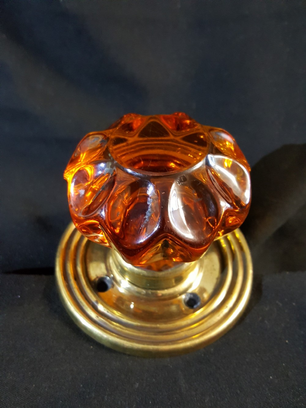 A Victorian amber glass door knob with a faceted profile mounted on a circular stepped brass backplate. View VI