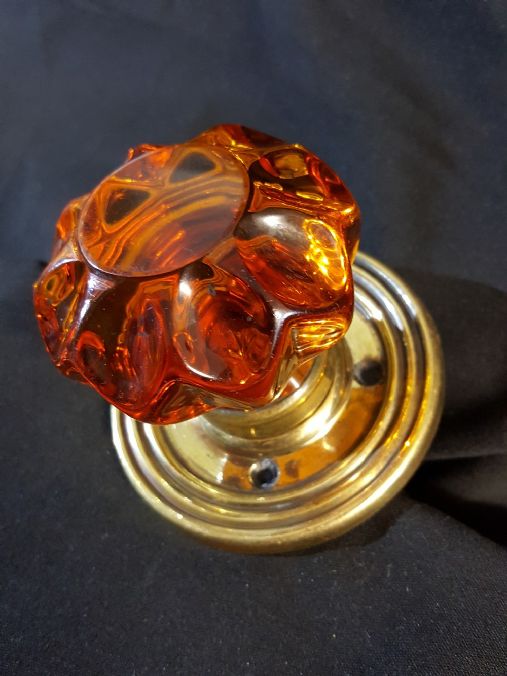 A Victorian amber glass door knob with a faceted profile mounted on a circular stepped brass backplate. View VII
