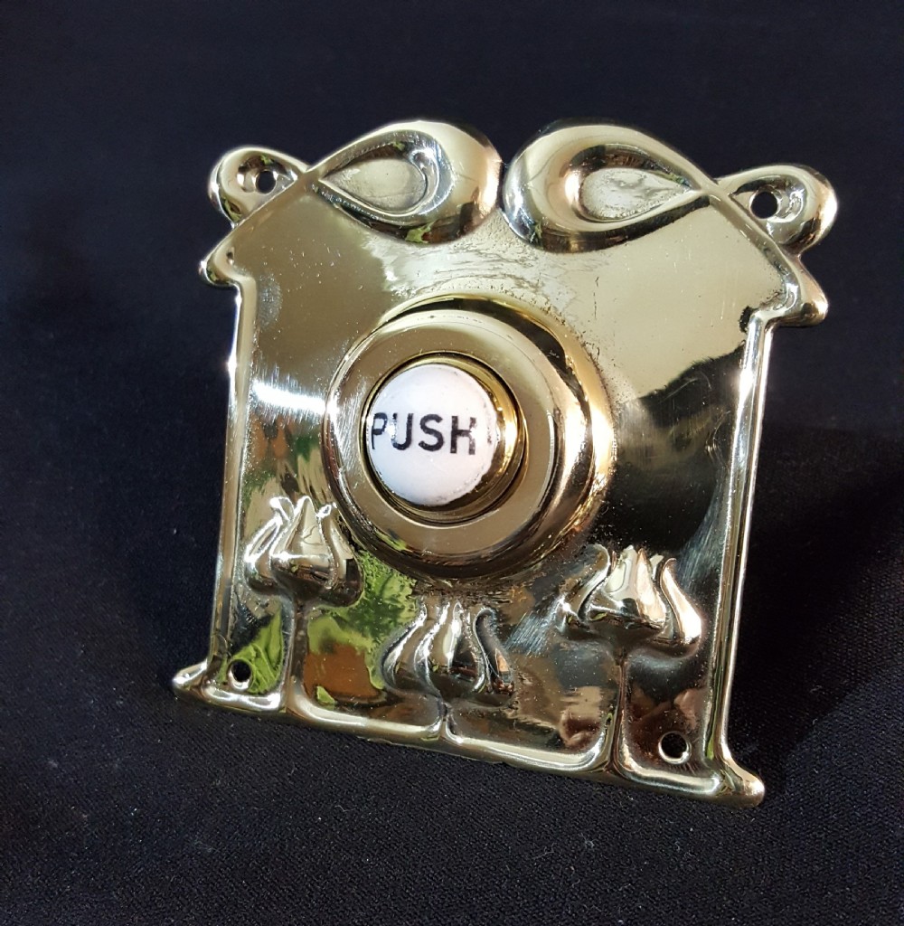 A square polished brass Art Nouveau bell push featuring stylised botanical relief motifs and a central white porcelain button with the word PUSH printed in black. View V