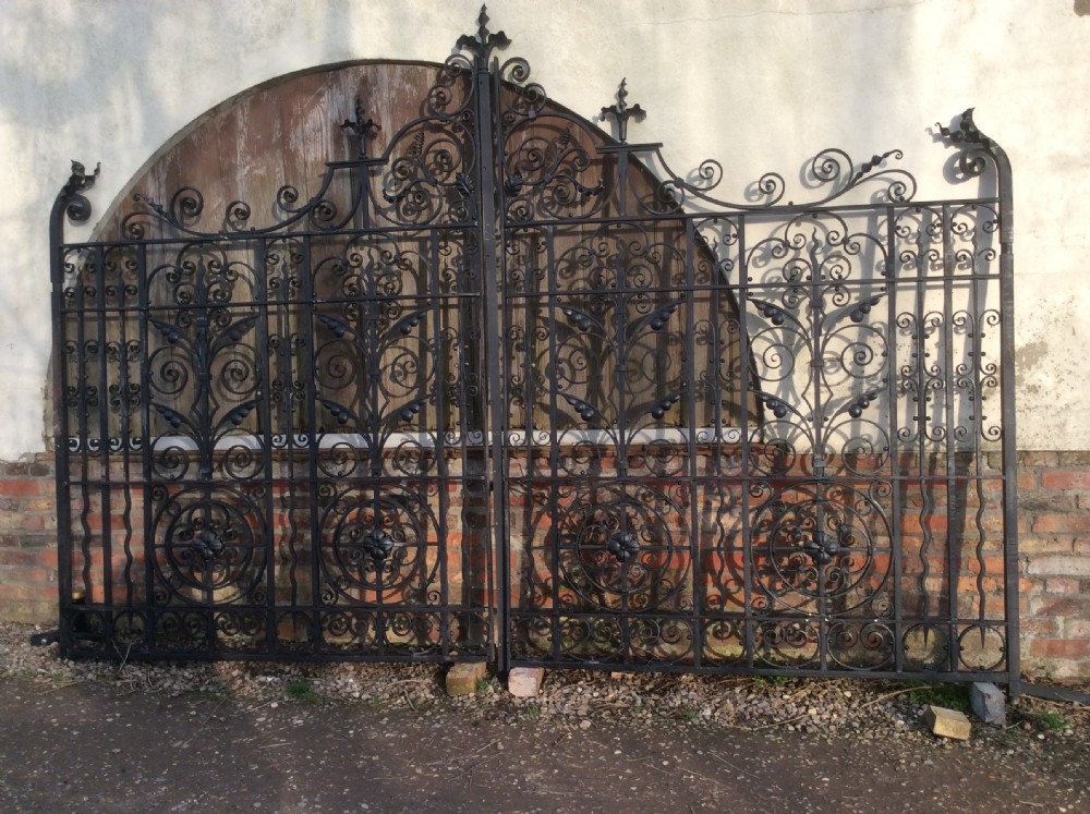 A pair of large black Victorian wrought iron driveway gates featuring ornate scrollwork, circular medallions, and decorative top finials.