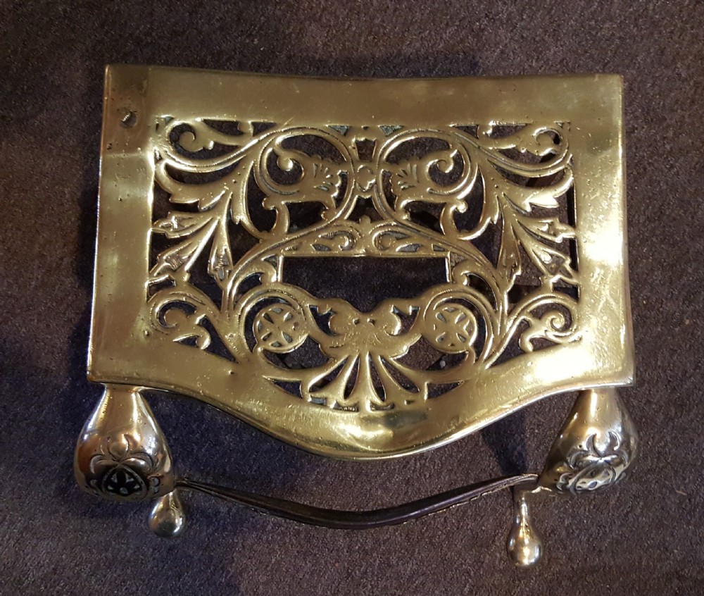 A Georgian pierced brass hearth footman featuring acanthus foliage scrollwork, side carrying handles, and shaped front cabriole legs.
