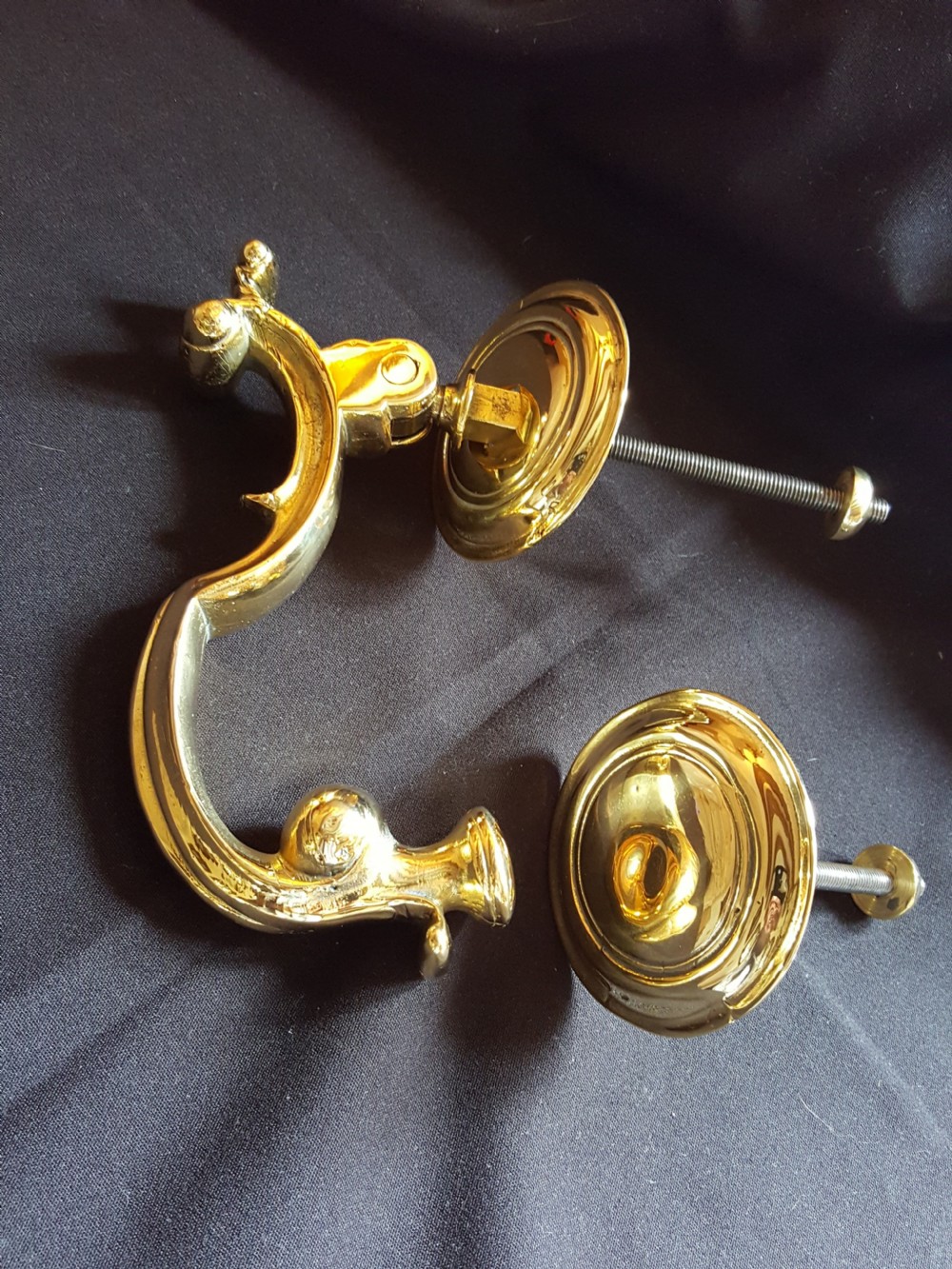 A polished brass Doctors style door knocker featuring an S-shaped handle and threaded mounting bolts.