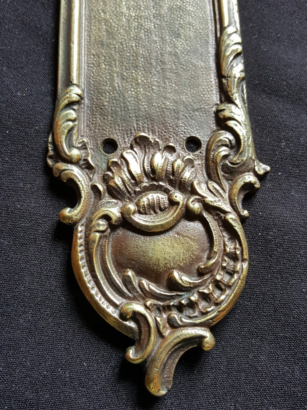 A single cast brass Georgian style finger plate displaying scrollwork and cartouche relief detailing at top and bottom ends. View III
