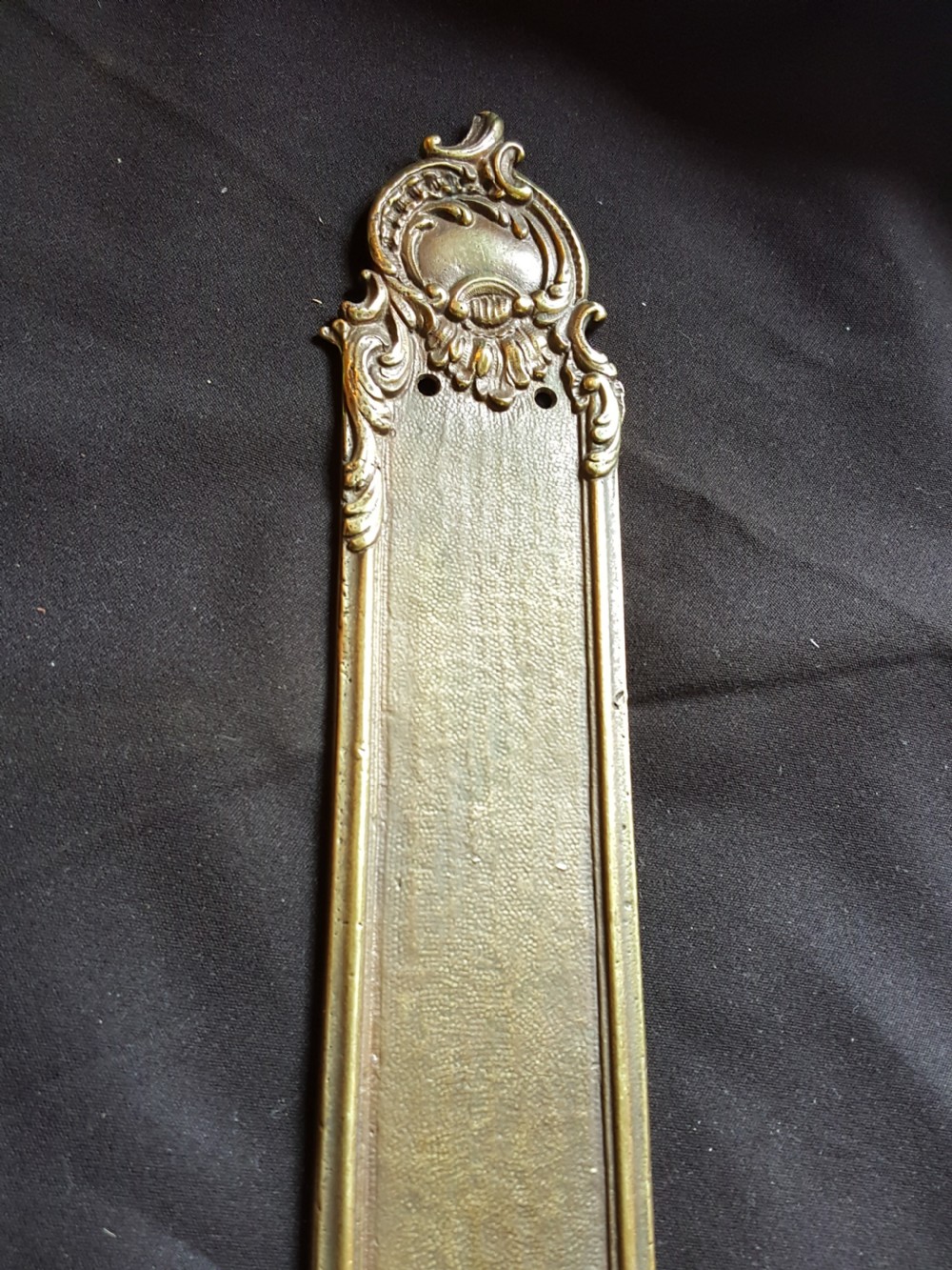 A single cast brass Georgian style finger plate displaying scrollwork and cartouche relief detailing at top and bottom ends. View VII