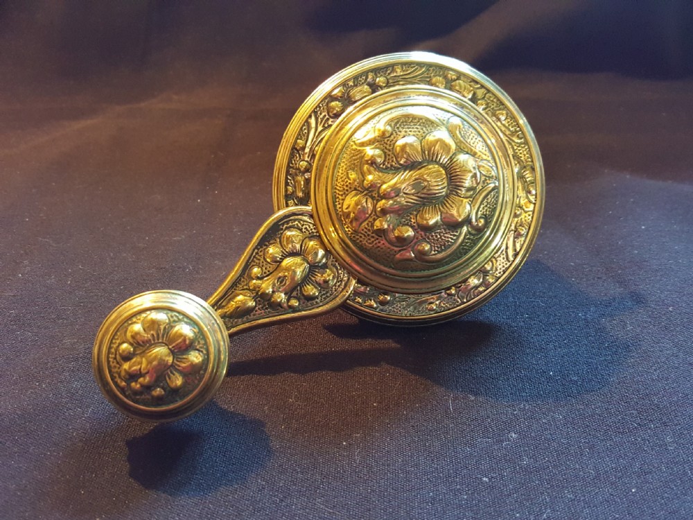 An ornate Victorian brass bell ringer featuring elaborate embossed floral patterns and a mechanical turn lever.