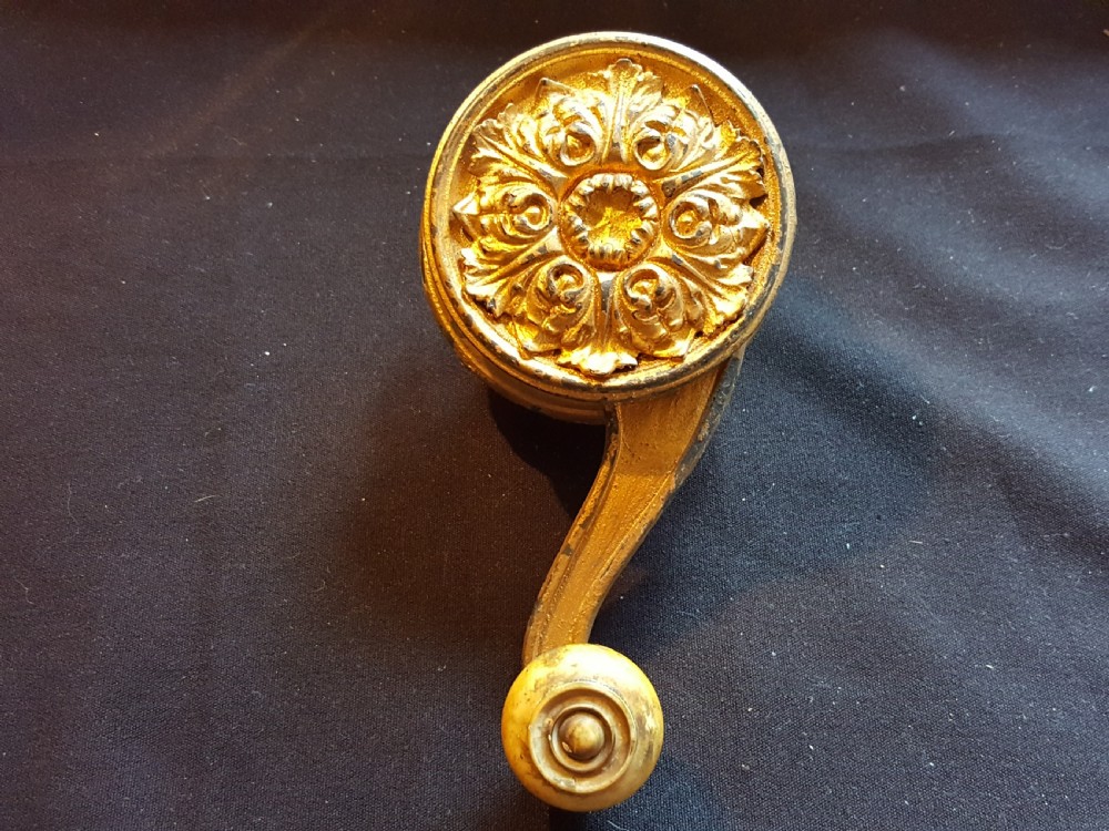 An ornate Georgian gilt brass mechanical bell pull featuring a circular carved floral rosette and a curved lever arm.