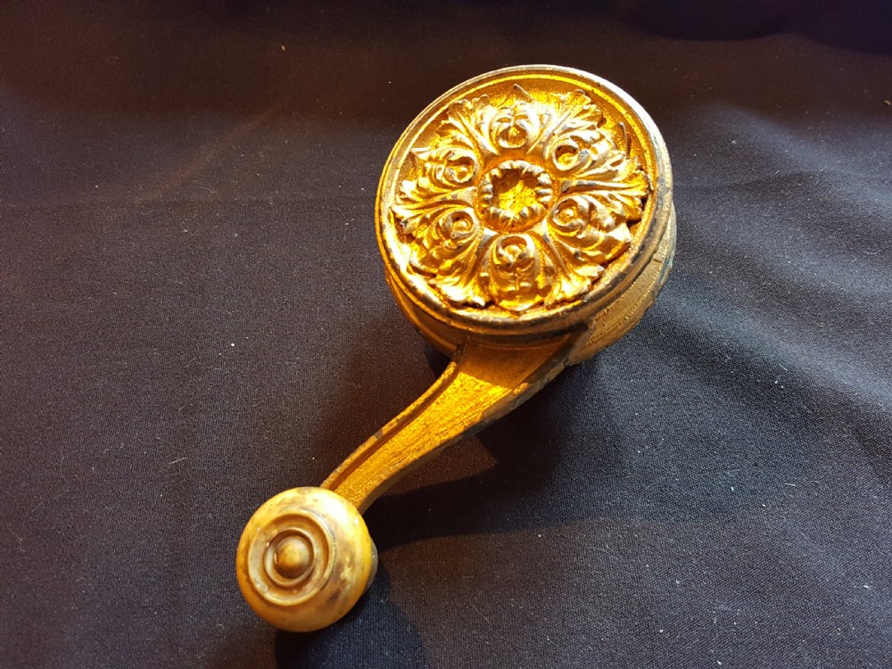 An ornate Georgian gilt brass mechanical bell pull featuring a circular carved floral rosette and a curved lever arm. View II
