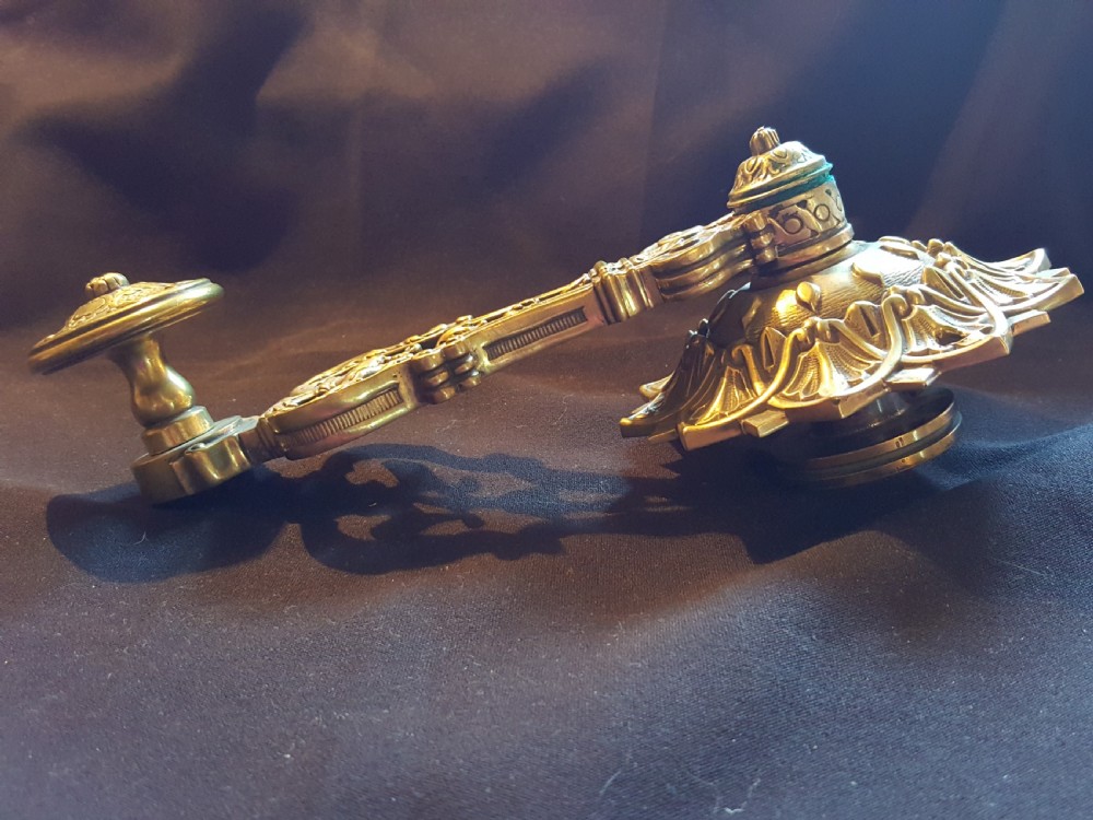 An ornate cast brass mechanical wall-mounted bell ringer featuring a sunburst rosette top, openwork scrollwork with mythical creatures, and a circular decorative pendulum drop. View III