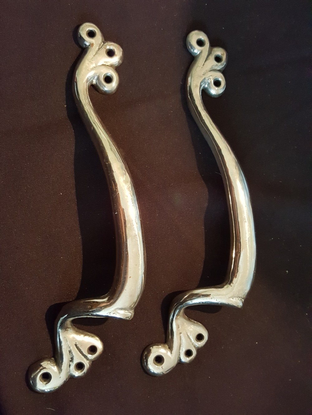 A pair of polished metal Art Nouveau door pull handles featuring curved whiplash forms with scrolled mounting plates.