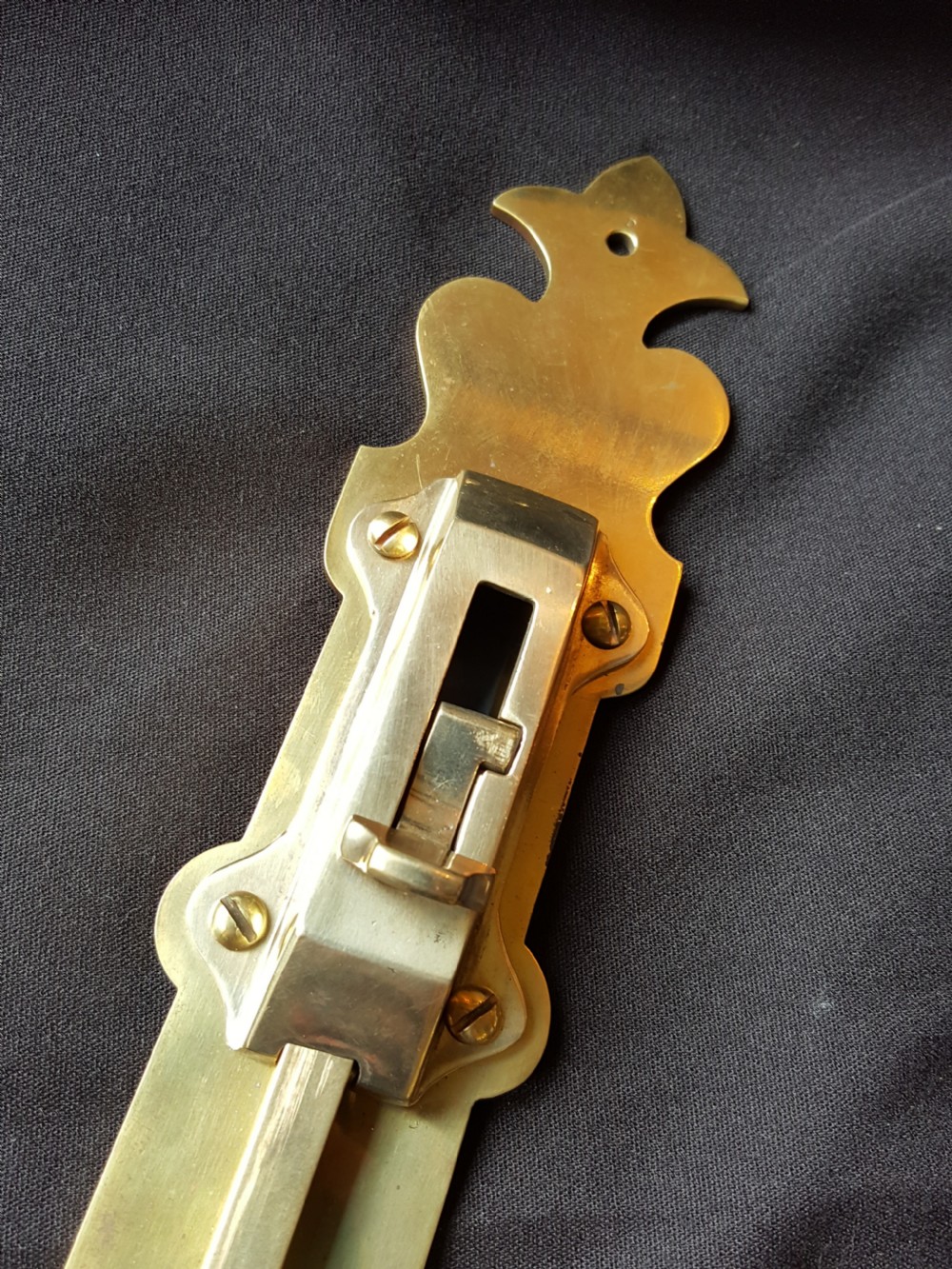 A Victorian Gothic Revival solid brass surface door bolt with a decorative shaped backplate, trefoil cutouts, and a matching keeper. View II