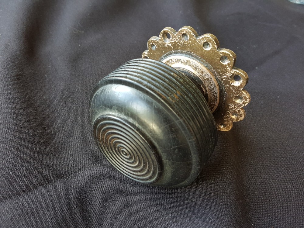 A Victorian centre door knob featuring a turned black ebony head with concentric circular grooves attached to a scalloped brass rose.