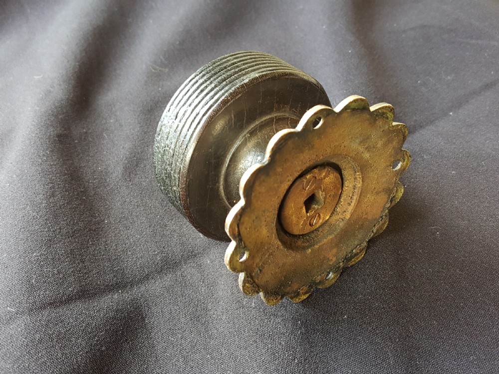 A Victorian centre door knob featuring a turned black ebony head with concentric circular grooves attached to a scalloped brass rose. View V
