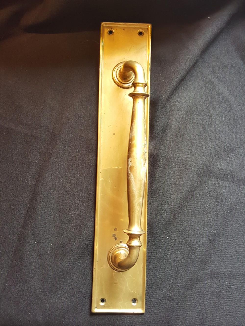 A solid brass Edwardian door pull handle mounted on a rectangular backplate with four corner mounting holes.