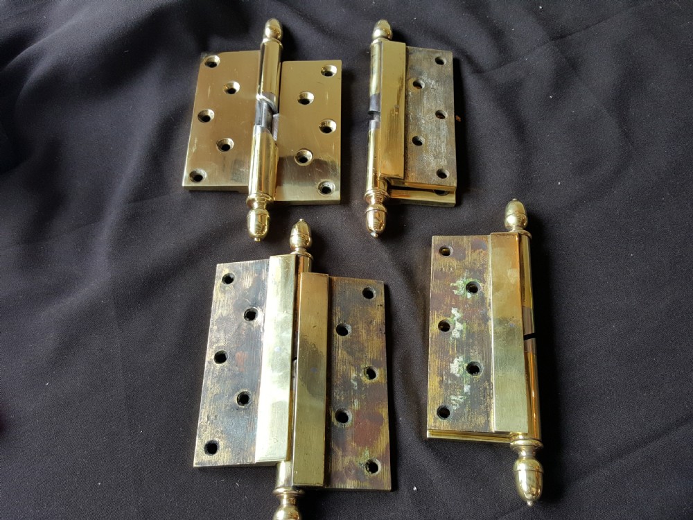 A set of four heavy cast brass Victorian door hinges featuring decorative acorn finials and pre-drilled countersunk screw holes with natural patina.