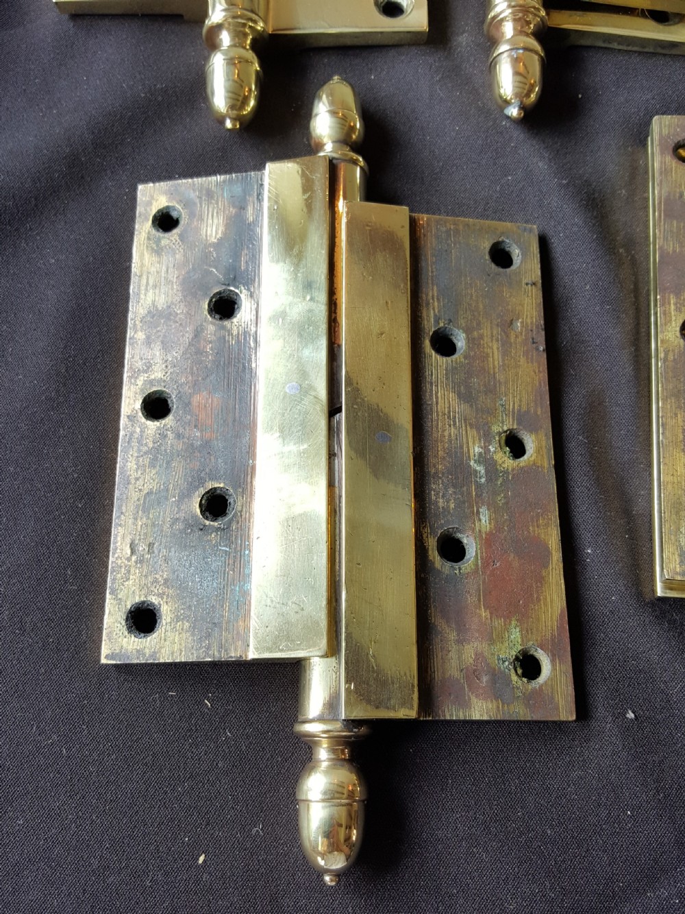 A set of four heavy cast brass Victorian door hinges featuring decorative acorn finials and pre-drilled countersunk screw holes with natural patina. View II