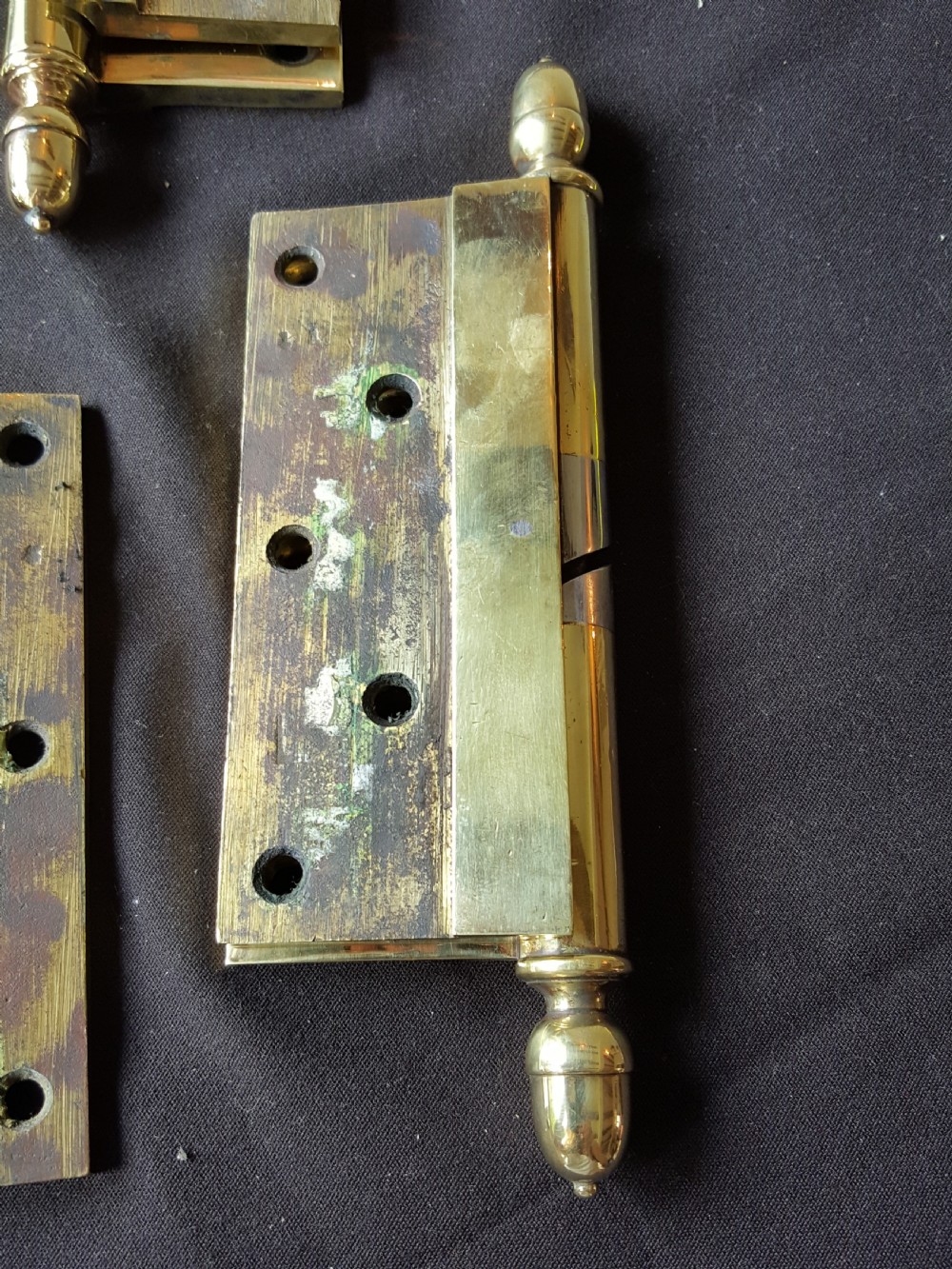 A set of four heavy cast brass Victorian door hinges featuring decorative acorn finials and pre-drilled countersunk screw holes with natural patina. View III