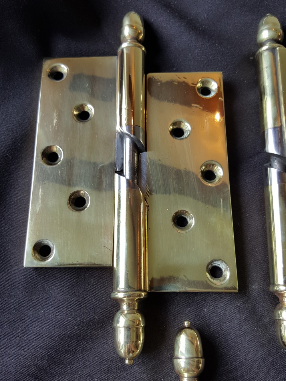 A set of four heavy cast brass Victorian door hinges featuring decorative acorn finials and pre-drilled countersunk screw holes with natural patina. View V