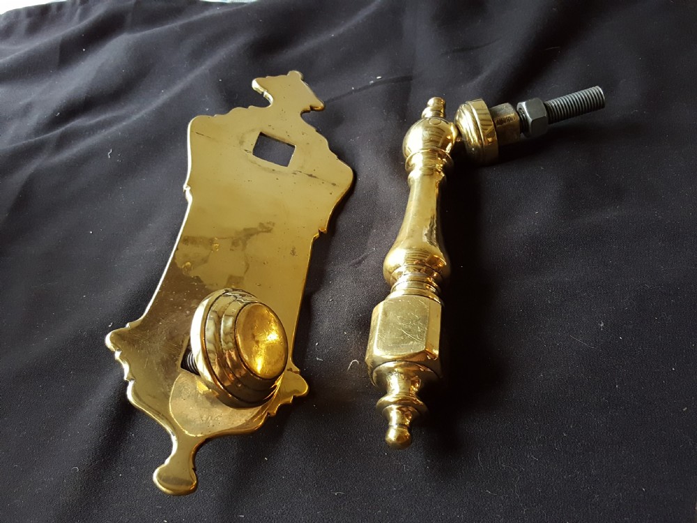 A two-piece Victorian polished brass door knocker comprising a shaped backplate with a striking stud and a turned baluster-style knocker with a threaded bolt.