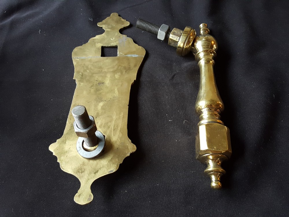 A two-piece Victorian polished brass door knocker comprising a shaped backplate with a striking stud and a turned baluster-style knocker with a threaded bolt. View V