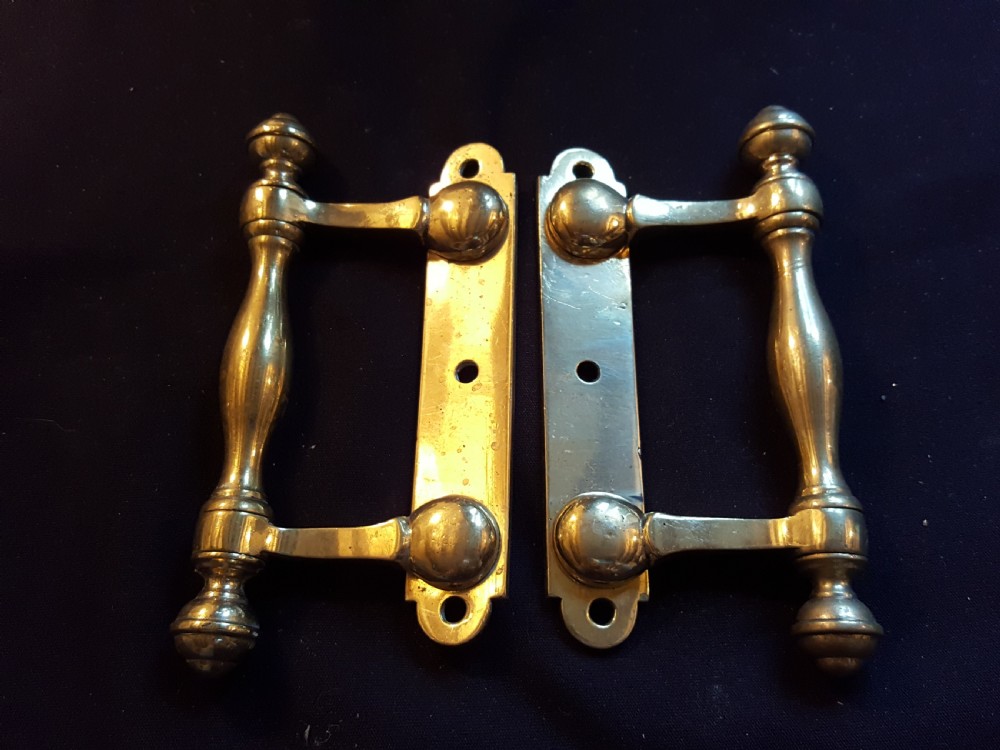 A pair of cast Victorian brass sash lifts featuring turned baluster handles with finials attached to flat mounting plates with screw holes.