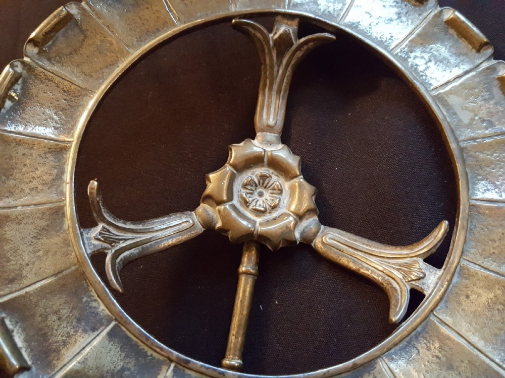 A circular Victorian brass kettle stand trivet featuring a fluted rim design and a central three-spoke motif. View III