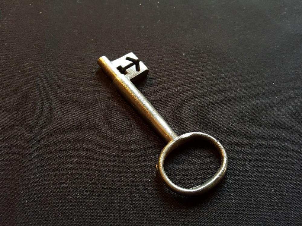 An antique Georgian cast steel key with an oval bow and a notched bit resting on a dark fabric surface.