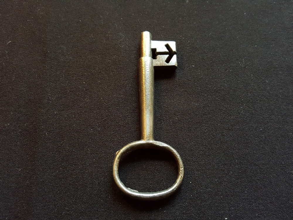 An antique Georgian cast steel key with an oval bow and a notched bit resting on a dark fabric surface. View II