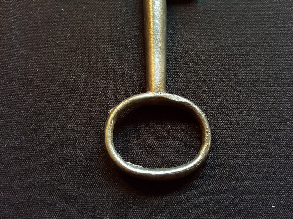 An antique Georgian cast steel key with an oval bow and a notched bit resting on a dark fabric surface. View III