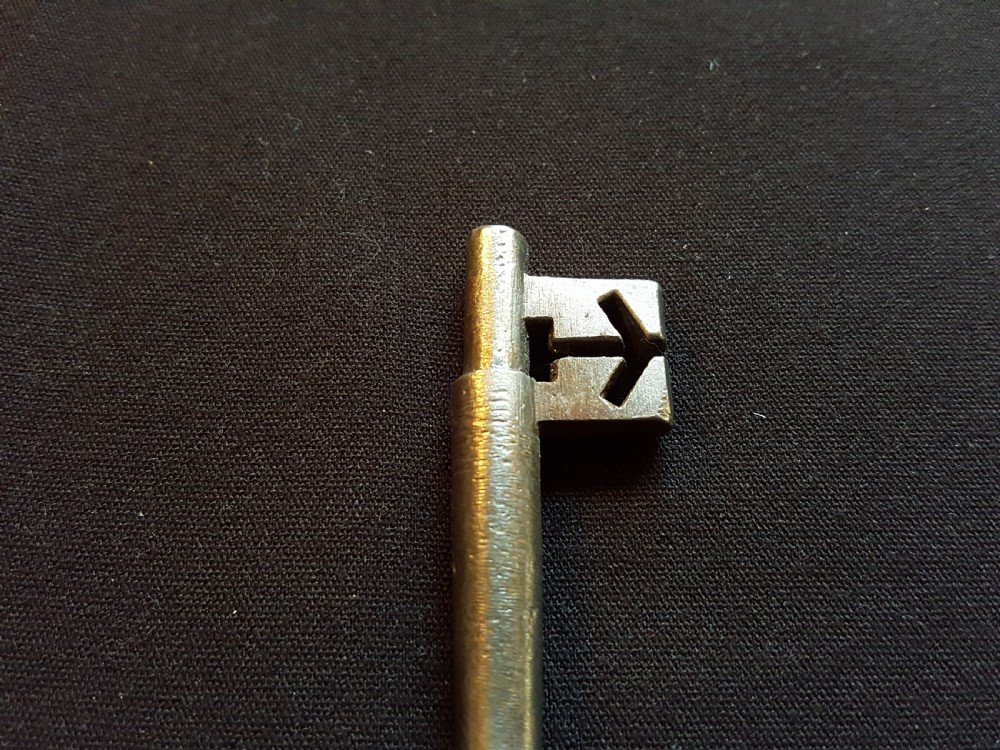 An antique Georgian cast steel key with an oval bow and a notched bit resting on a dark fabric surface. View IV