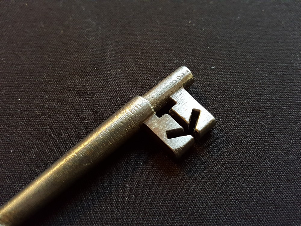 An antique Georgian cast steel key with an oval bow and a notched bit resting on a dark fabric surface. View V