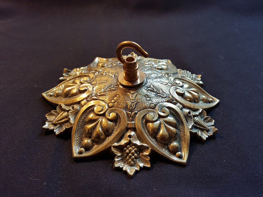 An ornate circular Victorian cast brass ceiling rose featuring relief foliage decoration and a central hanging hook.