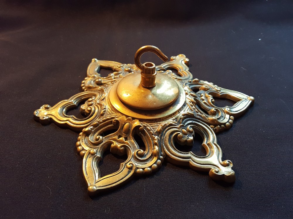 A Victorian cast brass ceiling rose featuring a central metal hook surrounded by openwork scrollwork and a starburst edge profile.